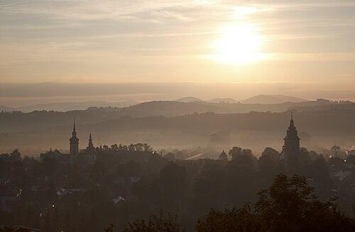 Stary Sącz za svítání – siluety kláštera a farního kostela nad mlhou